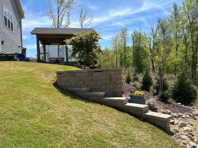 Backyard slope with stone retaining wall, steps, and a covered patio beside a house