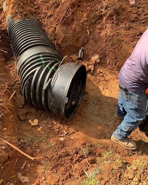 Black drainage pipe in a dirt trench, with a worker crouching beside it.