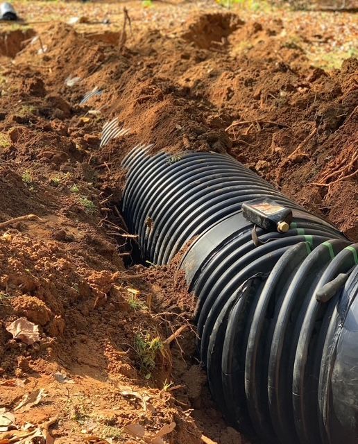 Black corrugated drainage pipe laid in a dirt trench at a construction site