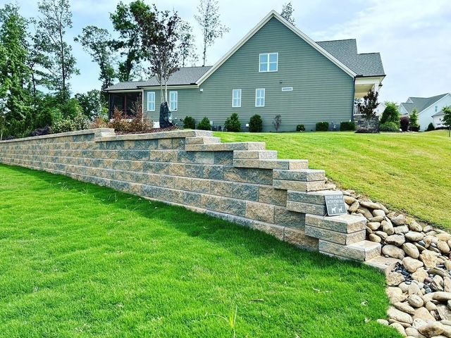 Retaining wall and stone steps on a grassy slope beside a gray house