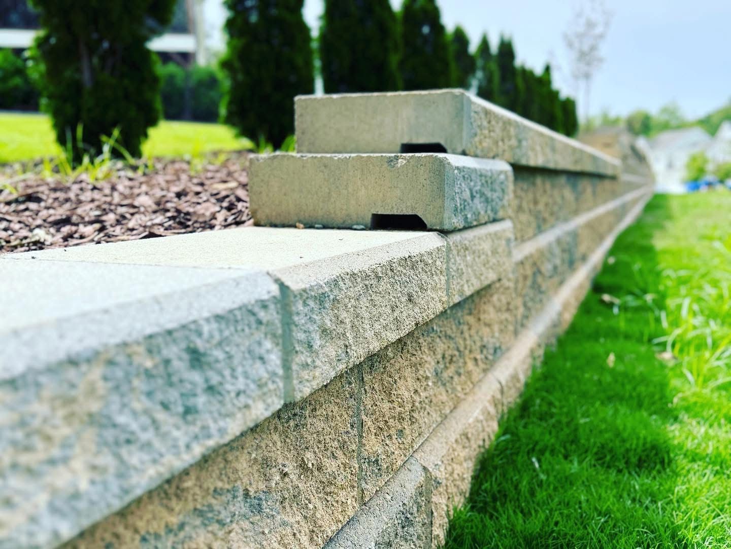 Gray stone retaining wall beside green grass and shrubs in a landscaped yard