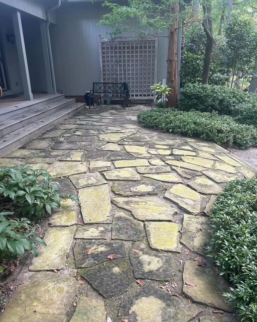 Stone pathway leading to a house porch, bordered by greenery and trees