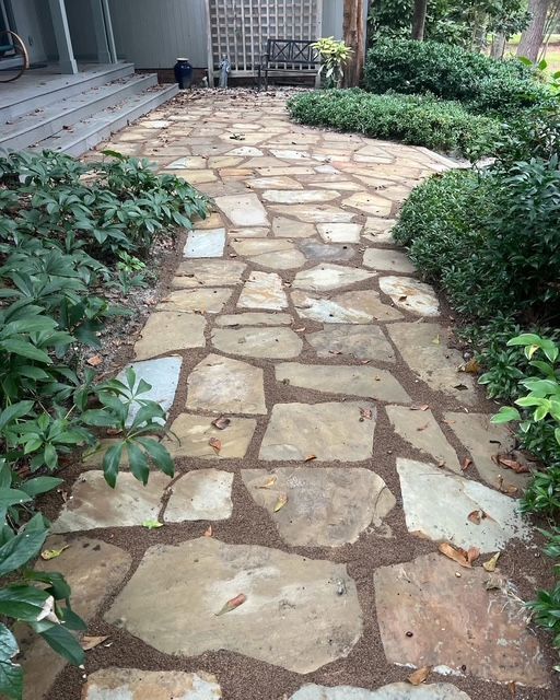 Stone garden path bordered by green shrubs leading to a house patio