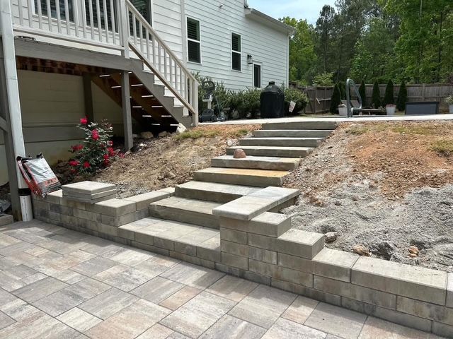 Front yard stone stairway and retaining wall beside a house, with paver patio and sloped landscaping