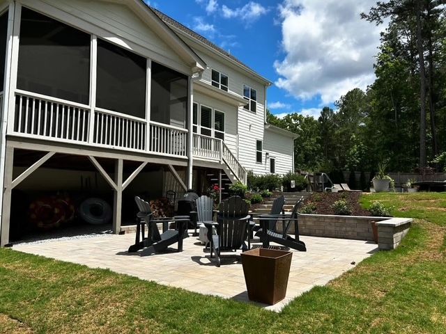 Backyard patio with outdoor chairs, fire pit, porch, and landscaped lawn beside a house under a blue sky