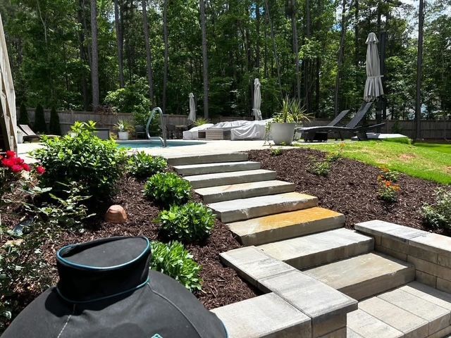 Backyard patio with stone steps, lounge chairs, and lush landscaped garden surrounded by trees