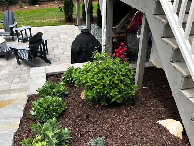 Backyard patio with chairs, stairs, and a landscaped flower bed with green shrubs and pink blooms