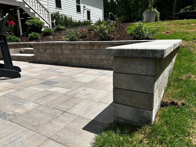 Stone patio with retaining wall and grassy yard beside a house