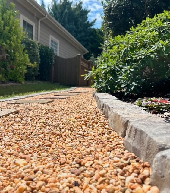 Gravel garden path beside a stone border and green shrubs next to a house