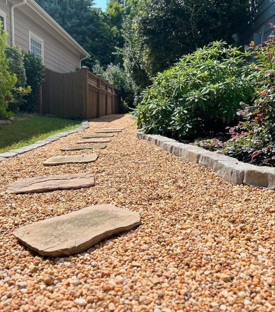 Pebble garden path with flat stepping stones beside a house and raised flower bed in sunlight
