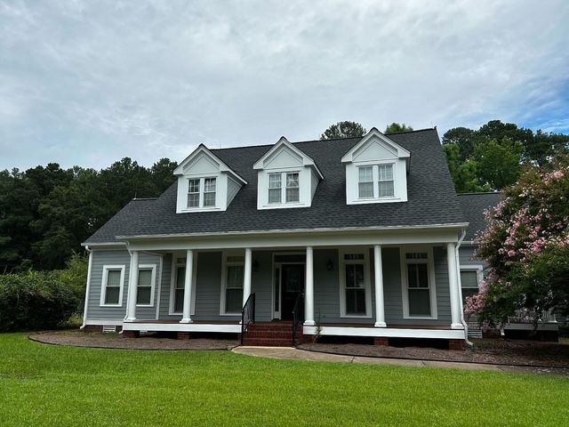 Gray house with white trim, dormer windows, and a front porch on a green lawn