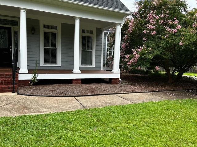 Front porch with white columns, brick steps, and a pink flowering tree beside a green lawn