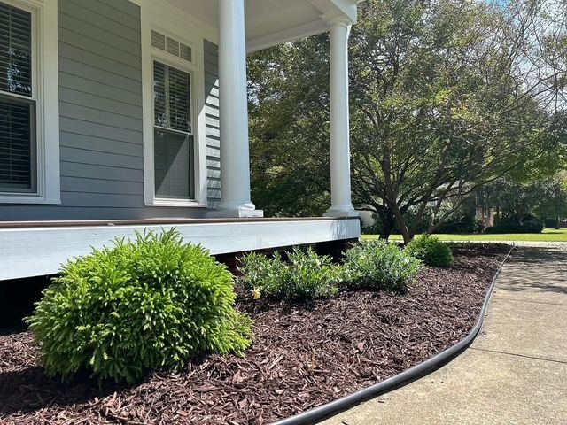 Front porch with white siding, windows, shrubs, and a curved mulch bed along a walkway.