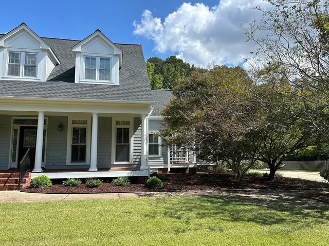 White house with dormer windows, front porch, and large green lawn under a blue sky