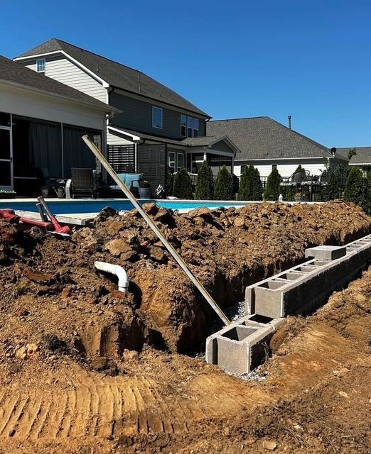 Backyard construction site with dug trench, cinder blocks, and a house in the background