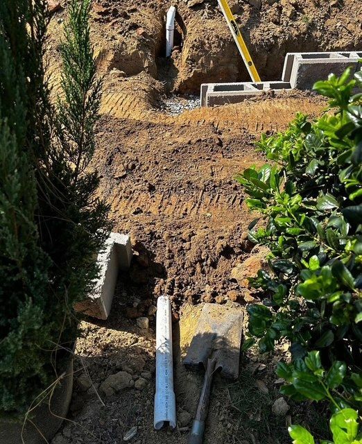 Dirt excavation area with a trench, concrete blocks, and pipes in a garden or yard