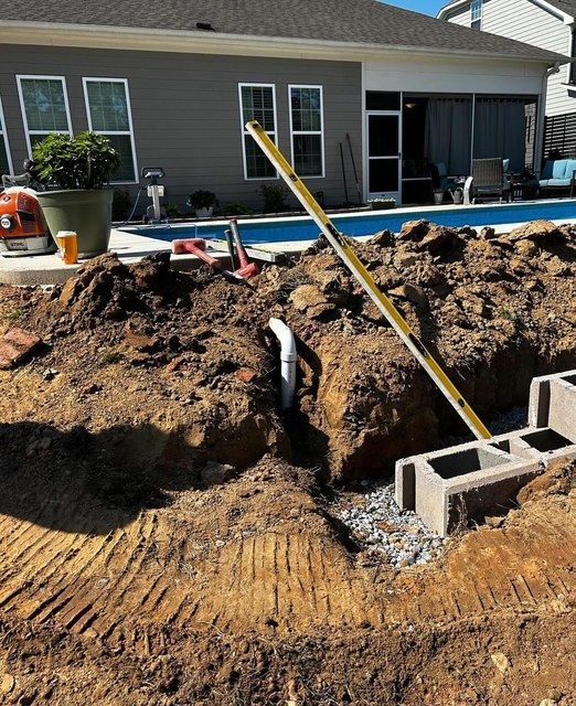 Backyard excavation beside a house with exposed dirt, cinder blocks, and construction tools around a pool area