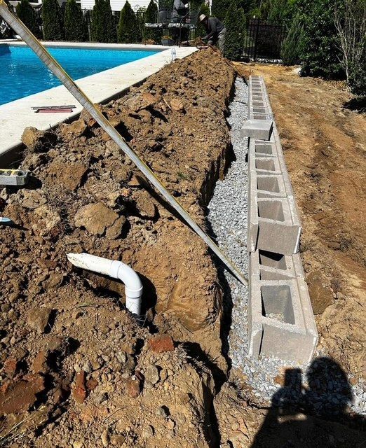 Swimming pool edge excavation with exposed pipe and cinder blocks beside a gravel trench