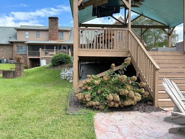 Backyard deck and stairs beside a house, with a large bush and patio seating area