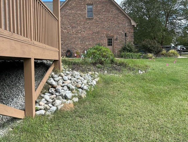Brick house with a wooden deck and stone landscaping beside a green lawn.