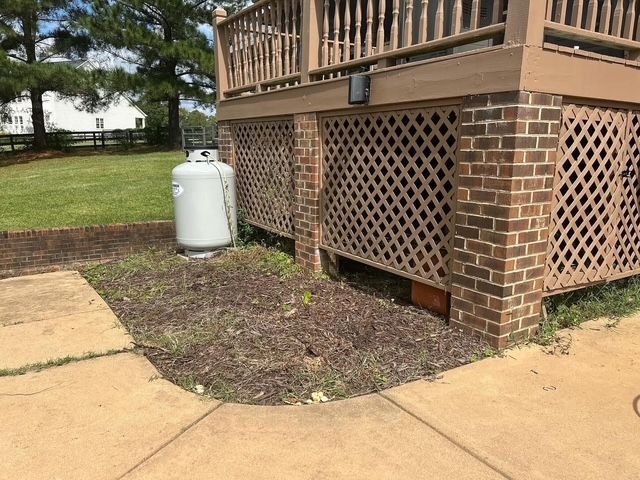 Brick house corner with tan lattice skirting, white propane tank, and concrete walkway