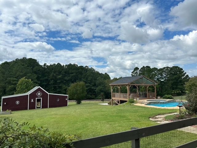 Rural yard with red barn, gazebo, and swimming pool under a cloudy sky