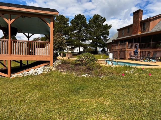 Backyard with wooden gazebo, poolside patio, lawn, and a brick house under a cloudy sky