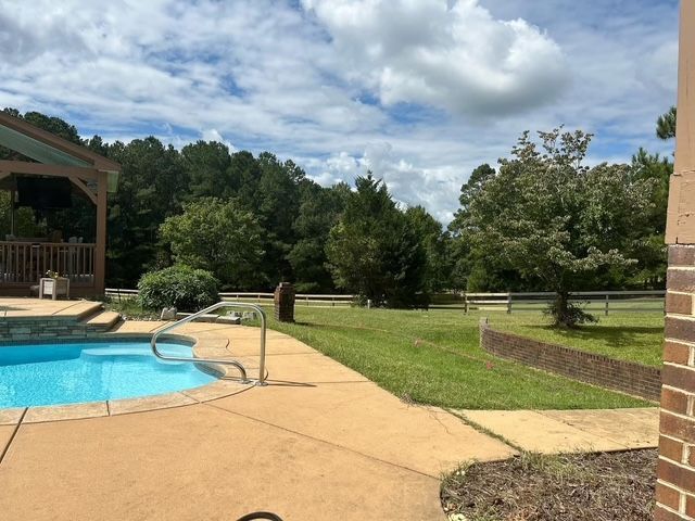 Backyard patio with a swimming pool, lounge chairs, and a grassy lawn under a partly cloudy sky