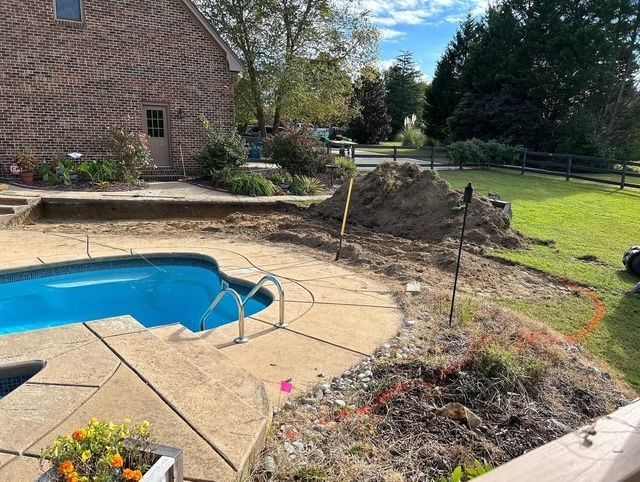 Backyard pool beside a brick house, with patio stones, garden beds, and lawn under a blue sky