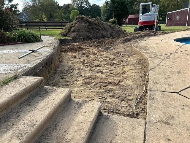 Excavated dirt path beside stone steps, with a small excavator and soil pile in a landscaped area