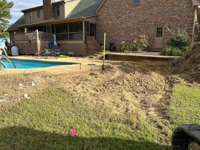 Backyard with a swimming pool, brick house, and a freshly graded dirt slope beside the patio