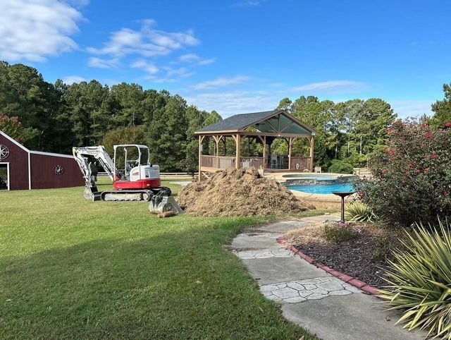 Backyard with gazebo, pool, red shed, and small excavator on the lawn under a blue sky