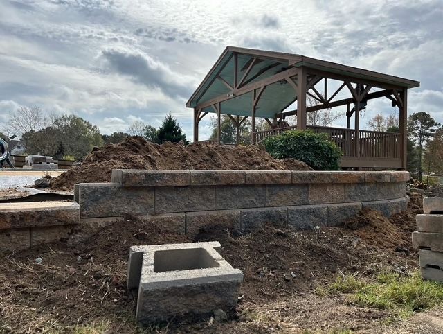 Partially built stone pavilion in a muddy, demolished outdoor area under a cloudy sky