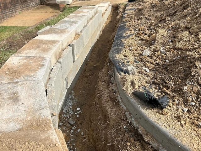 Trench dug beside a concrete retaining wall and curved dirt edge in a construction area