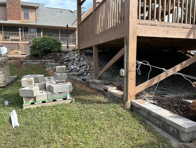 Backyard with stacked concrete blocks, grassy ground, and a wooden deck supported by posts and braces