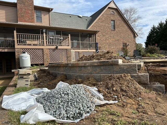 Backyard patio with stone retaining walls, gravel pile, and a house in the background
