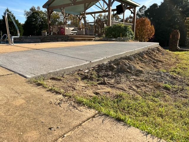 Concrete ramp beside a pavilion, with a steep dirt embankment and grassy area.