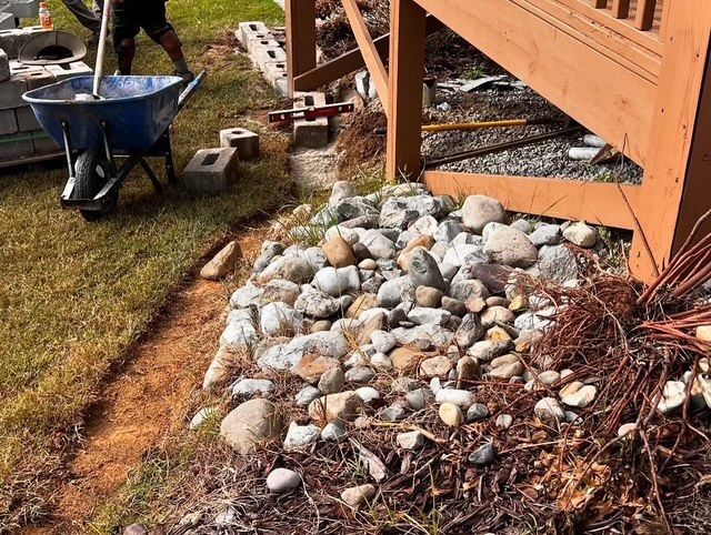 A wheelbarrow beside a rock bed next to a wooden deck in a yard.