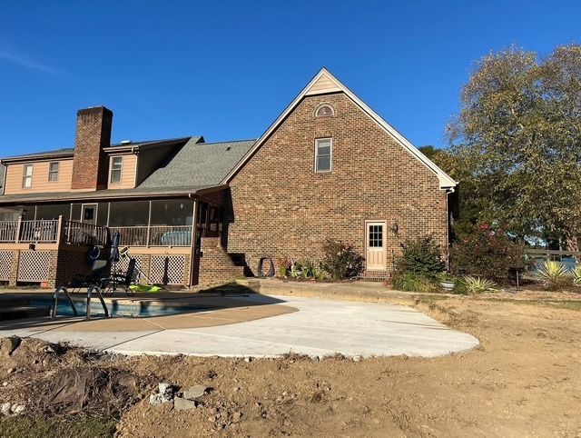 Brick house exterior with patio, pool area, and bare yard under a clear blue sky