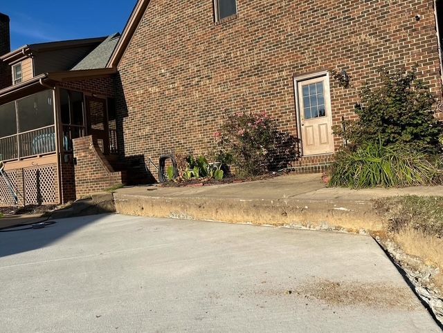 Brick house exterior with concrete driveway, front porch, and a white door in bright daylight