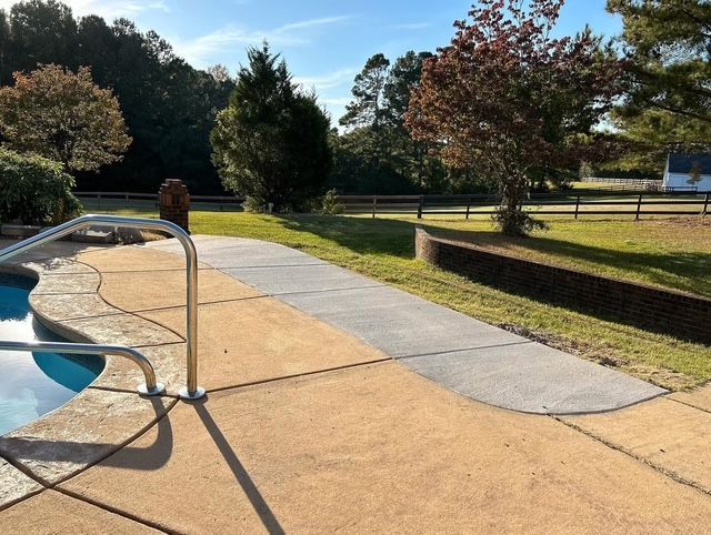 Pool deck with a metal handrail, curving walkway, grass, and trees in a sunny park setting