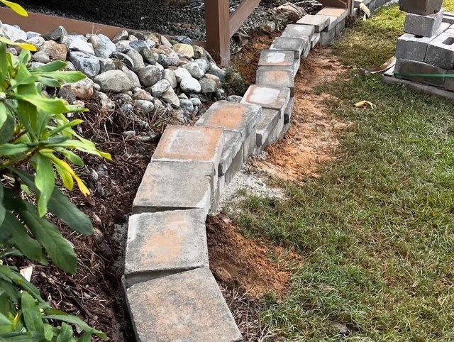 Curved concrete edging stones lining a garden bed beside rocks and grass