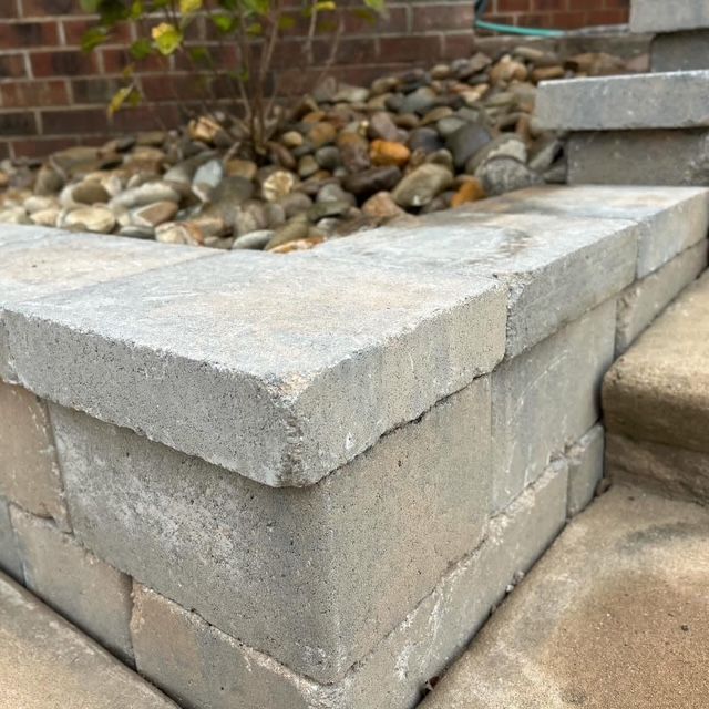 Gray concrete retaining wall corner beside a landscaped rock bed and brick wall