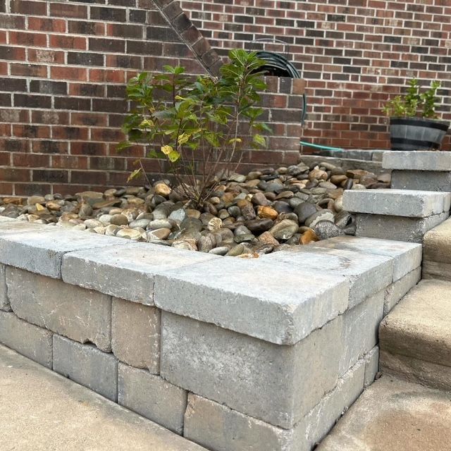 Small landscaped planter with rocks and a young shrub beside brick steps and wall