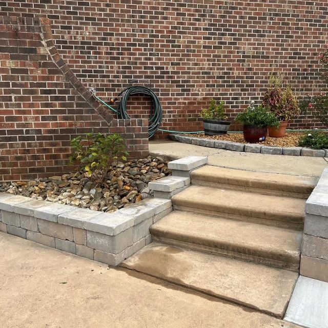 Brick steps beside a low retaining wall and landscaped garden against a brick house exterior.