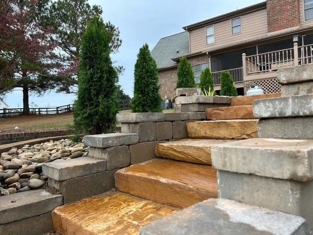 Stone steps with tan blocks leading to a house patio, bordered by retaining walls and landscaping