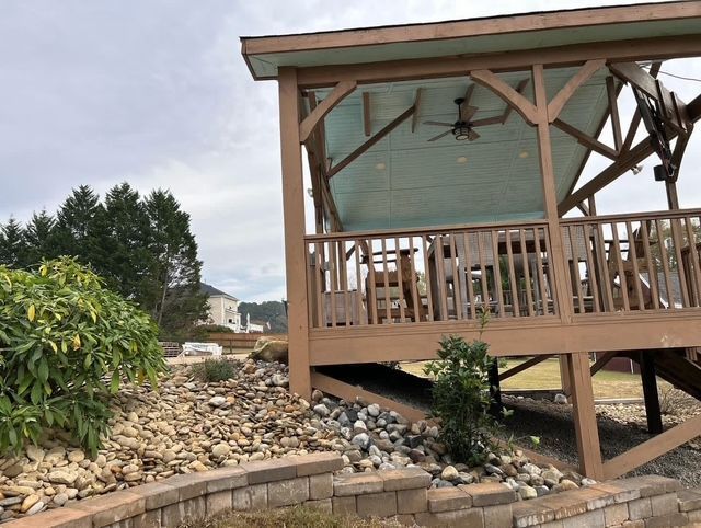 Wooden gazebo on a rocky slope with a porch, railing, and ceiling fan under a cloudy sky