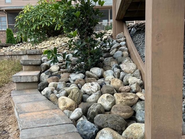 Stone landscape beside steps and a house, with a sloped bed of river rocks and shrubs