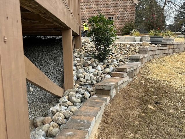 Backyard stone retaining wall with tiered steps, rocks, and a wooden deck edge on the left