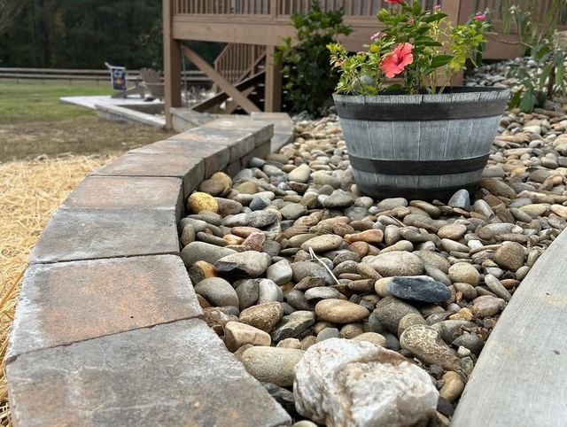 Curved stone border around a pebble garden with a wooden planter of pink flowers
